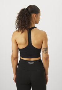 Fekete sportmelltartó, racerback kialakítással, textúrált pántokkal és testreszabott fazonban, fekete leggings-szel párosítva, amelyen a "VENUM" logó látható.