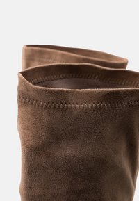 Ejes de botas de ante marrón hasta la rodilla con una textura suave y bordes cosidos, que presentan un diseño de parte superior plegada.