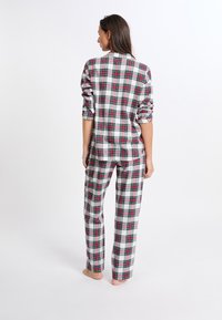 Ensemble de pyjama à carreaux comprenant une chemise à boutons avec des manches retroussées et un pantalon à jambe droite, dans des couleurs gris, blanc, rouge et vert. Tissu doux.