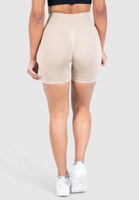 Beige hoge taille shorts met een gladde textuur, voorzien van een gestructureerd patroon op de achterkant en eindigend op middeldij, gecombineerd met witte sneakers.