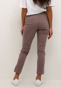 Jasnobrązowe, dopasowane spodnie o gładkiej fakturze, z tylnymi kieszeniami i podwiniętymi mankietami, zestawione z białymi trampkami.