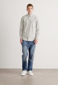 Lys grå, langermet skjorte med knapper og krage, sammen med blå denimjeans og hvite joggesko. Enkelt design, avslappet passform.