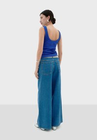 Blauw geribbeld tanktop en wijde denim jeans. De jeans hebben twee achterzakken en een licht verweerd textuur. Witte schoenen.