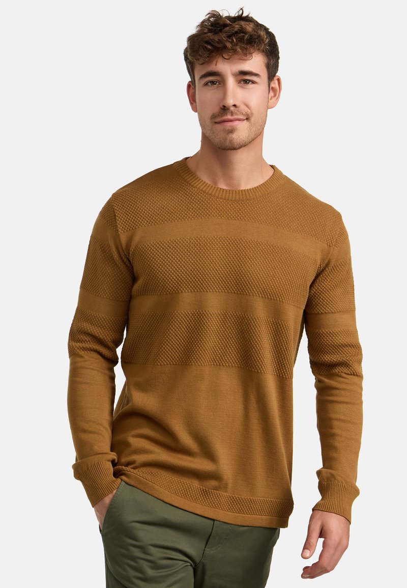Brun strikket genser med et teksturert mønster og horisontale striper. Lange ermer og rund hals. Kombinert med olivengrønne bukser.