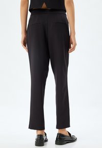 Pantalones negros de pierna recta que presentan una tela suave, dos bolsillos traseros y una cinturilla, combinados con zapatos negros tipo mocasín.