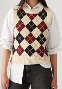 Gilet en tricot avec une base crème et un motif losanges multicolores en bordeaux, bleu marine et jaune. Encolure et ourlet côtelés, design sans manches.