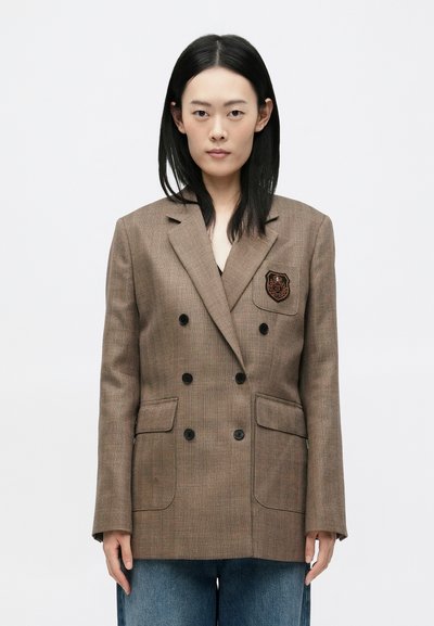 Braunes kariertes Doppelreiher-Blazer mit schwarzen Knöpfen, zwei Taschen und einem gestickten Abzeichen auf der Brust, taillierte Passform, glattes Material.