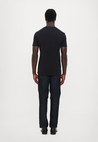 Svart kortermet T-skjorte kombinert med mørk denimjeans, sett fra baksiden. Slim fit, klassisk rund hals-design, jevn tekstur.