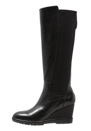 Botte compensée noire montante jusqu'au genou avec l'avant en cuir lisse et le panneau arrière en tissu extensible, bout arrondi et semelle en caoutchouc.