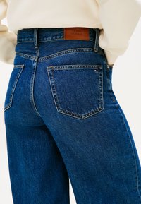 Ciemnoniebieskie jeansy z denimu o wysokim stanie, z brązową skórzaną metką z tyłu, dwoma tylnymi kieszeniami i subtelnymi detalami przeszyć.