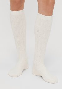 Knee-high socks in off-white, featuring a textured knit pattern, ribbed cuffs, and smooth footbed. Made from a soft yarn material.