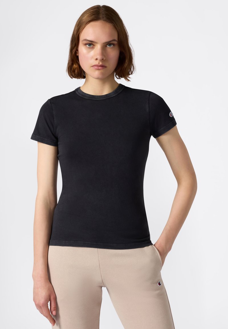 T-shirt nera aderente in tessuto morbido, con maniche corte e scollatura rotonda. Include un piccolo logo sulla manica sinistra.