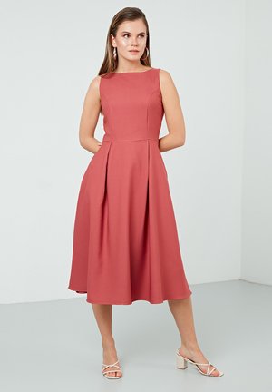 Une robe sans manches, longueur genou, dans une teinte corail, avec un corsage ajusté, des poches latérales et une jupe fluide avec des plis.