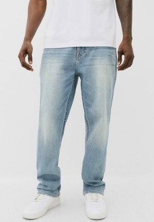 Jeans in denim azzurro chiaro con vestibilità rilassata, texture sbiadita e design a cinque tasche, abbinati a sneaker bianche.
