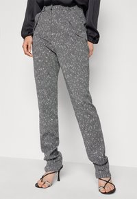 Pantalons gris à motif avec un design de petites taches, coupe slim, avec une taille haute et des poches latérales, associés à des sandales à talons hauts noires.