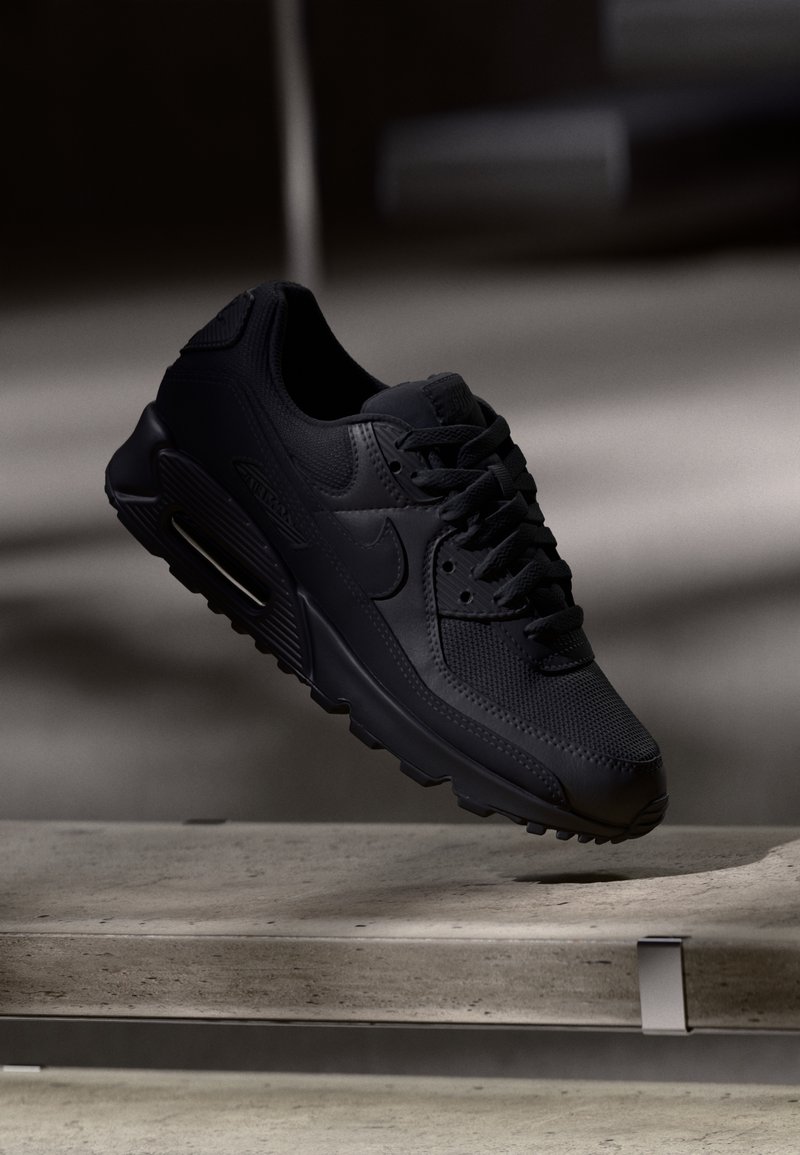 Mustade Nike Air Max 90 spordijalatsid, millel on tekstuuriga võrkkanga pealispind, siledad nahkaktsenti, pehme kaelus ja nähtav õhukaitse taldades.