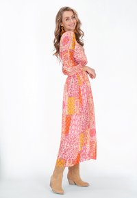 Langes, fließendes Kleid in einem lebhaften Patchwork aus pinken, orangen und gelben Mustern; durchsichtiger Stoff mit puffärmel und gerafftem Bund.