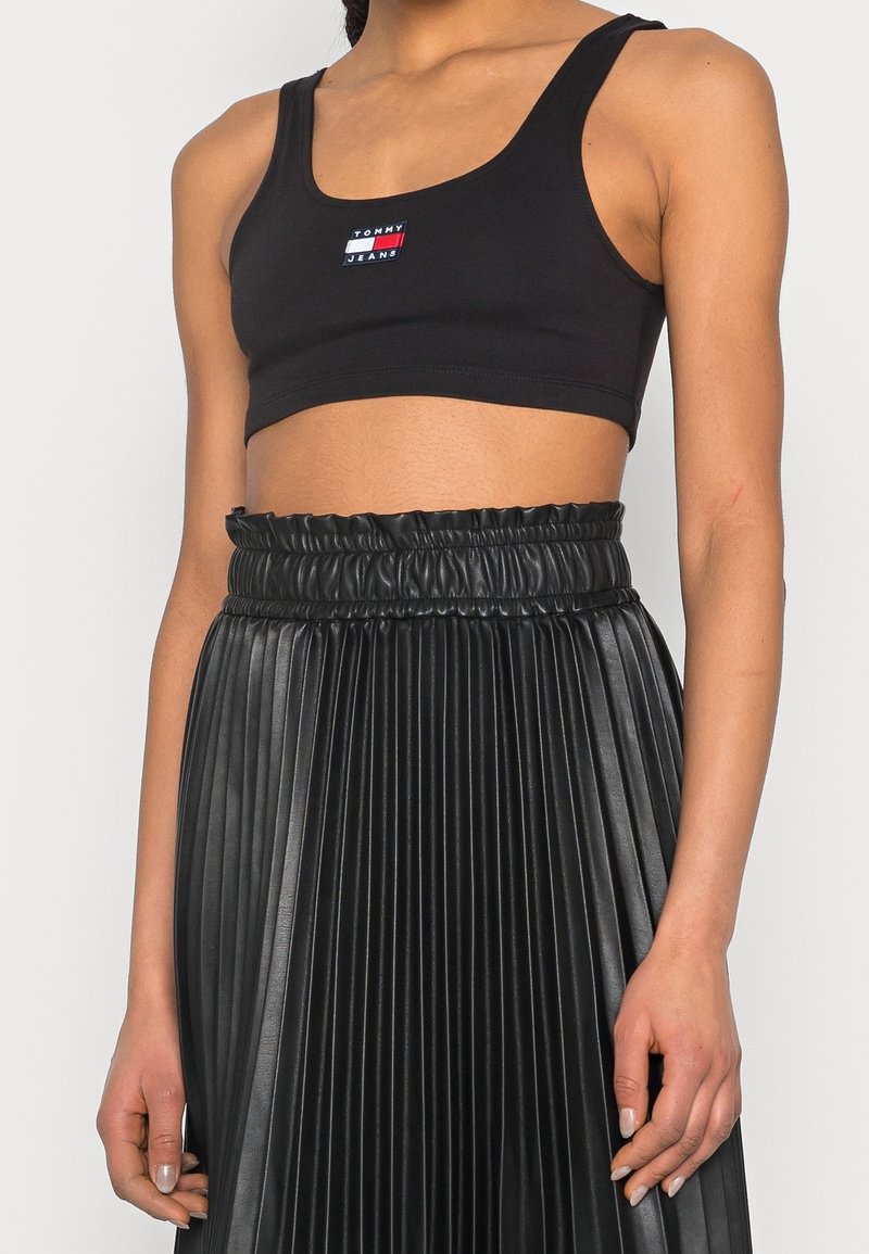 Svart cropped tanktop med en flerfärgad logotyp och en plisserad svart faux läderkjol med elastiskt midjeband.