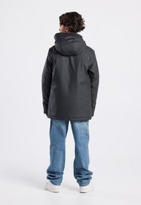 Black waterproof jacket with a hood, featuring a smooth texture and a relaxed fit. Paired with light blue, loose-fitting jeans and white shoes.