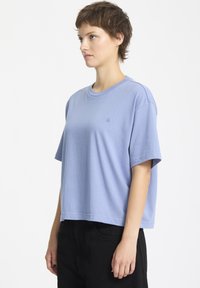 T-shirt azzurro chiaro a maniche corte realizzato in un tessuto morbido. Presenta un colletto a girocollo e un piccolo logo ricamato sulla parte sinistra del petto.