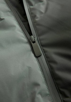 Mørkegrønne polstrede jakker lavet af stof med en glat overflade, der har en sort lynlås langs åbningen og fremhæver syningens detaljer.