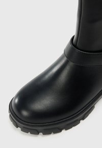 Juodos odinės batai su apvaliu pirštu, tekstūruota paviršiumi ir akcentuota guma padais, turinčiu tvirtą raštą.