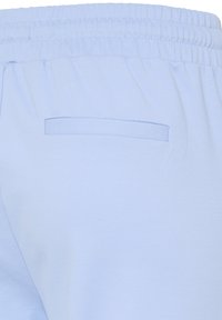 Gaiši zili bikses ar elastīgu jostasvietu un vienu šuvētu aizmugurējo kabatu labajā pusē.