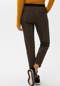 Pantalon à carreaux marron avec une ceinture noire, une coupe fuselée et deux poches arrière. Associé à des chaussures noires avec une semelle blanche.