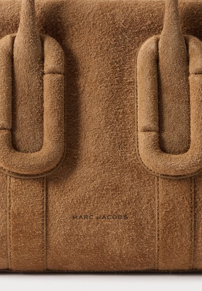 Gros plan d'un sac en daim marron montrant deux sangles en boucle et le logo Marc Jacobs embossé à l'avant.