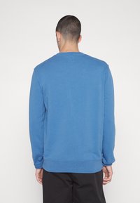 Felpa di cotone blu con maniche lunghe, scollo tondo e vestibilità comoda. Presenta orlo e polsini a coste, una trama liscia e nessun motivo visibile.