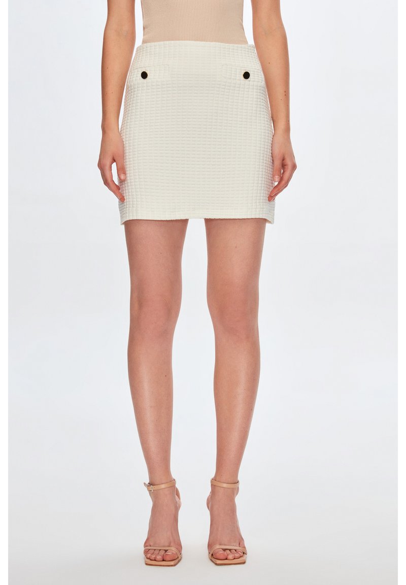 Witte textuur mini rok met twee voorzakken en zwarte knopen. De stof heeft een subtiel geweven patroon, wat zorgt voor een gestructureerde uitstraling.