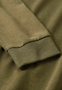 Olivovo zelený dlhý rukáv s detailmi na manžetách, vyrobený z jemnej, hladkej tkaniny, s čistým a jednoduchým dizajnom.