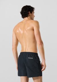 Črne kopalne kratke hlače iz lahkega materiala z elastičnim pasom, zadnjim žepom in logotipom na desni strani.