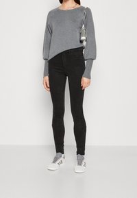 Suéter gris de manga larga con mangas abullonadas, combinado con jeans skinny negros. El calzado incluye zapatillas blancas con detalles y cordones grises.