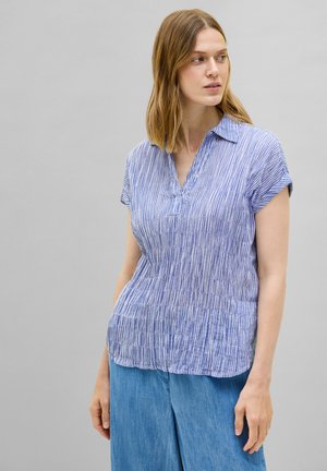 Blouse à manches courtes rayée en bleu et blanc, avec un col classique et une coupe décontractée en tissu légèrement texturé. Associée à un denim clair.