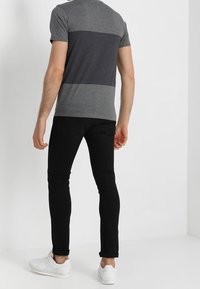 Camisa de rayas gris y gris oscuro de manga corta, combinada con jeans negros ajustados y zapatillas blancas, vista desde la parte posterior.