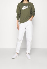 Olivgrön sweatshirt med vit Nike-logga, vita avslappnade byxor och vita sneakers. Tyget ser slätt och mjukt ut.