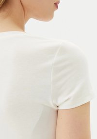 T-shirt a maniche corte crema chiaro con una texture morbida e liscia. Presenta un classico collo a giro e spalle aderenti; nessun motivo o design visibile.