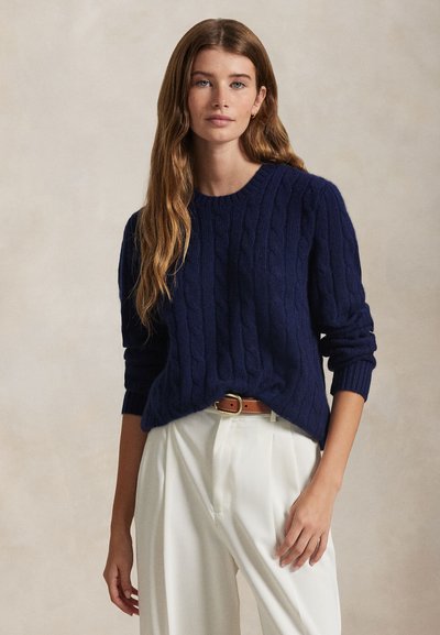 Μπλε ναυτικό πλεκτή ζακέτα με μακριά μανίκια και στρογγυλή λαιμόκοψη, συνδυασμένη με λευκό παντελόνι ψηλόμεσο και καφέ ζώνη.