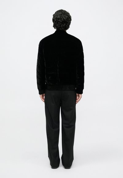 Μαύρο βελούδινο σακάκι με υψηλό γιακά και ριμπ μανσέτες, συνδυασμένο με μαύρο παντελόνι. Λεία υφή με κομψό, μινιμαλιστικό σχεδιασμό.