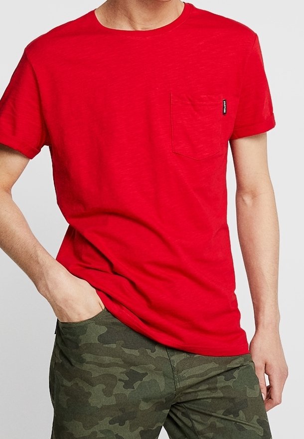 Rød bomulds T-shirt med rund halsudskæring og korte ærmer, der har en lomme på venstre bryst og et lille mærke. Bæres med camouflagebukser.