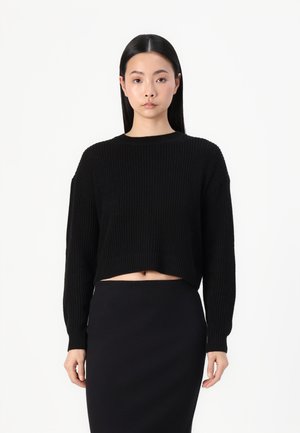 Black cropped sweater with ribbed texture, round neckline, and long sleeves, paired with a fitted black skirt.
