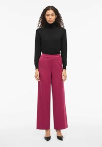 Pull noir à col roulé associé à un pantalon large magenta. Talons noirs pointus. Texture lisse, design minimaliste et coupe ajustée.