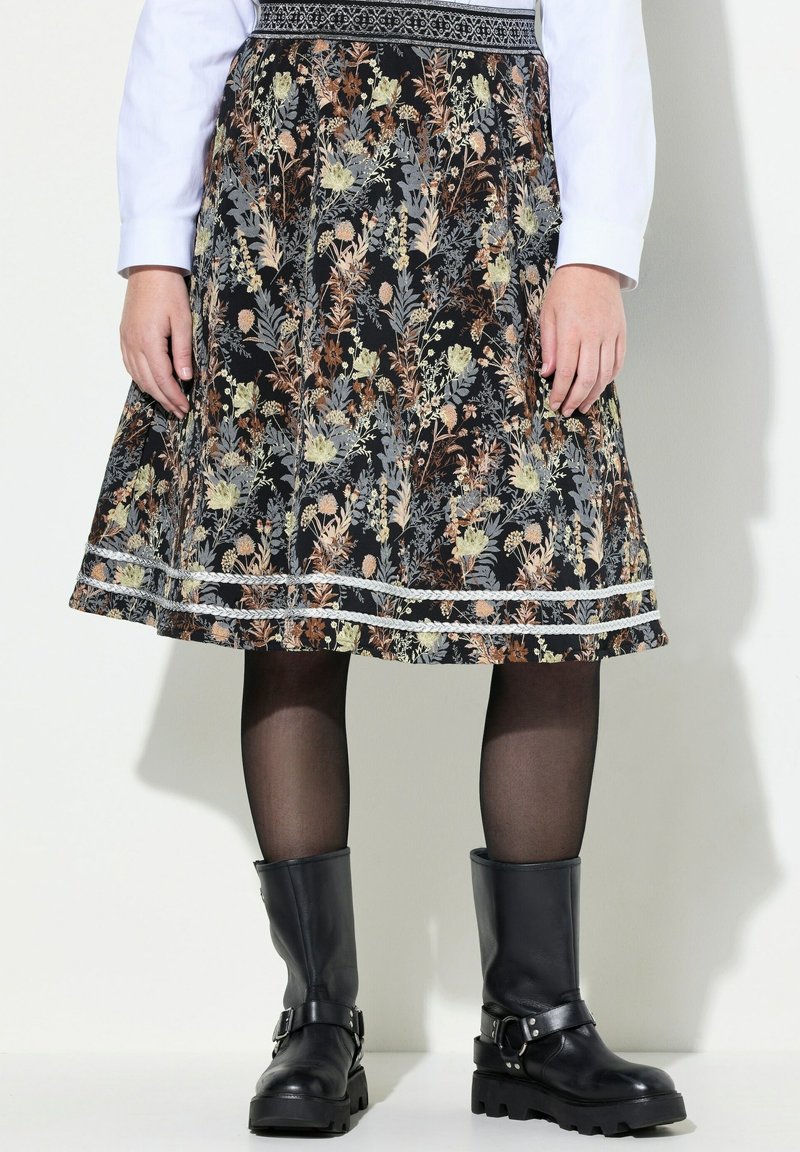 Jupe à motif floral longueur genou avec bordure en dentelle, associée à des collants noirs transparents et des bottes en cuir noir à boucle.