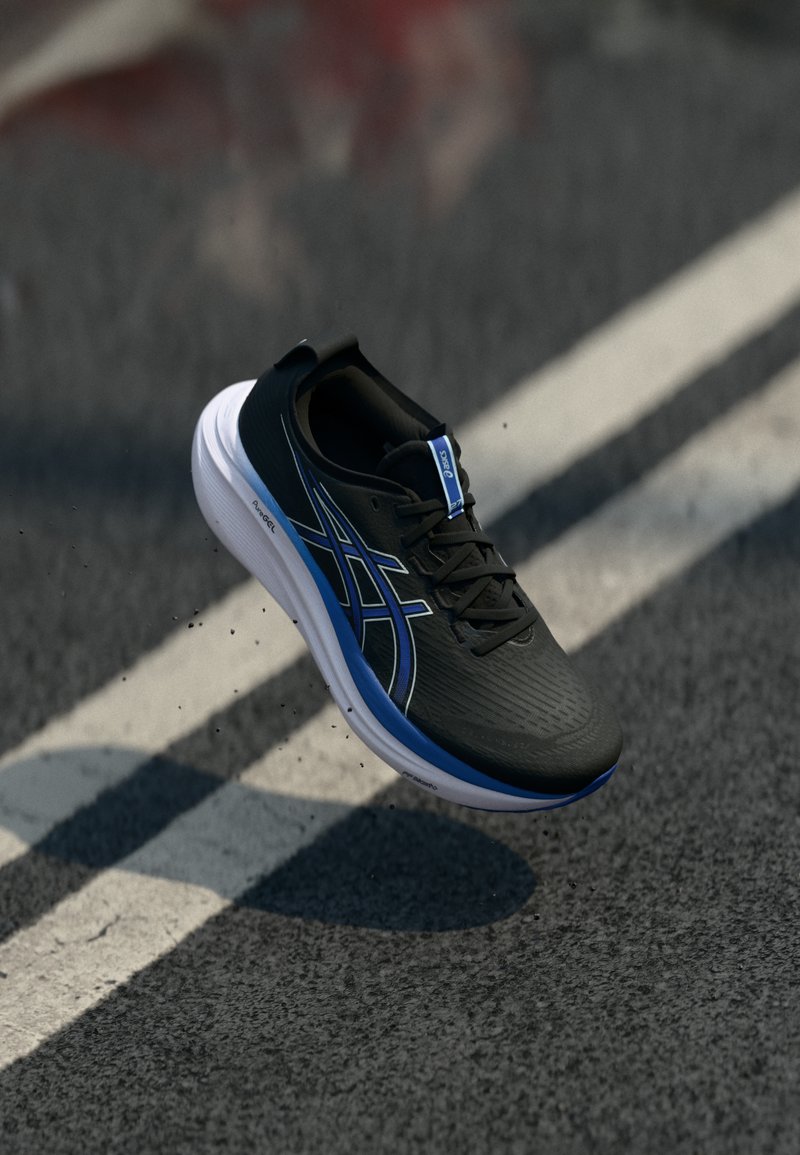 Chaussure de sport noire avec une tige texturée, accents bleus et une semelle blanche, présentée en plein vol au-dessus d'une surface grise avec des marquages routiers.