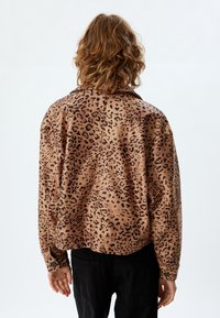 Leopardskinnjacka i brunt och svart, tillverkad av mjukt material. Har en avslappnad passform och långa ärmar, med en rundad nederkant baktill.