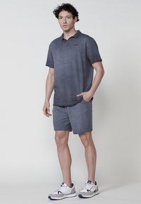 Polo shirt gris foncé à manches courtes et tissu texturé, associé à un short gris assorti et des baskets blanches avec des accents marine.