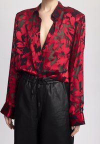 Rode en zwarte bloempatron blouse van doorschijnende stof met een diepe V-hals en knoopsluiting, gecombineerd met zwarte leren high-waisted broeken.