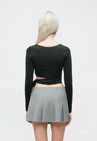 �Μακρυμάνικη σκούρα πράσινη μπλούζα με detail δέσιμο στο πίσω μέρος, συνδυασμένη με ανοιχτό γκρι πλισέ μίνι φούστα. Λείο ύφασμα σε όλη την επιφάνεια.