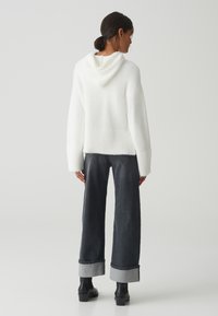 Weiße, flauschige Strickkapuze mit einer Rückennaht und Kapuze. Kombiniert mit hoch geschnittenen, dunklen Jeans mit aufgerollten Säumen und Ankle Boots.